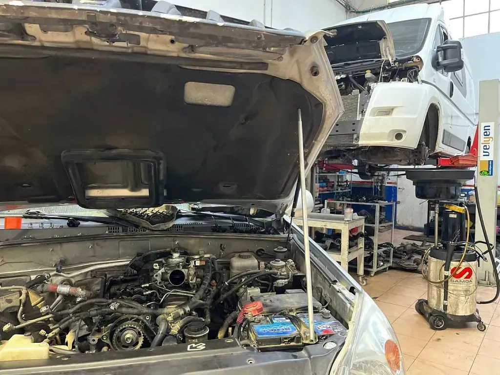 Un coche está siendo reparado en un garaje con el capó abierto.