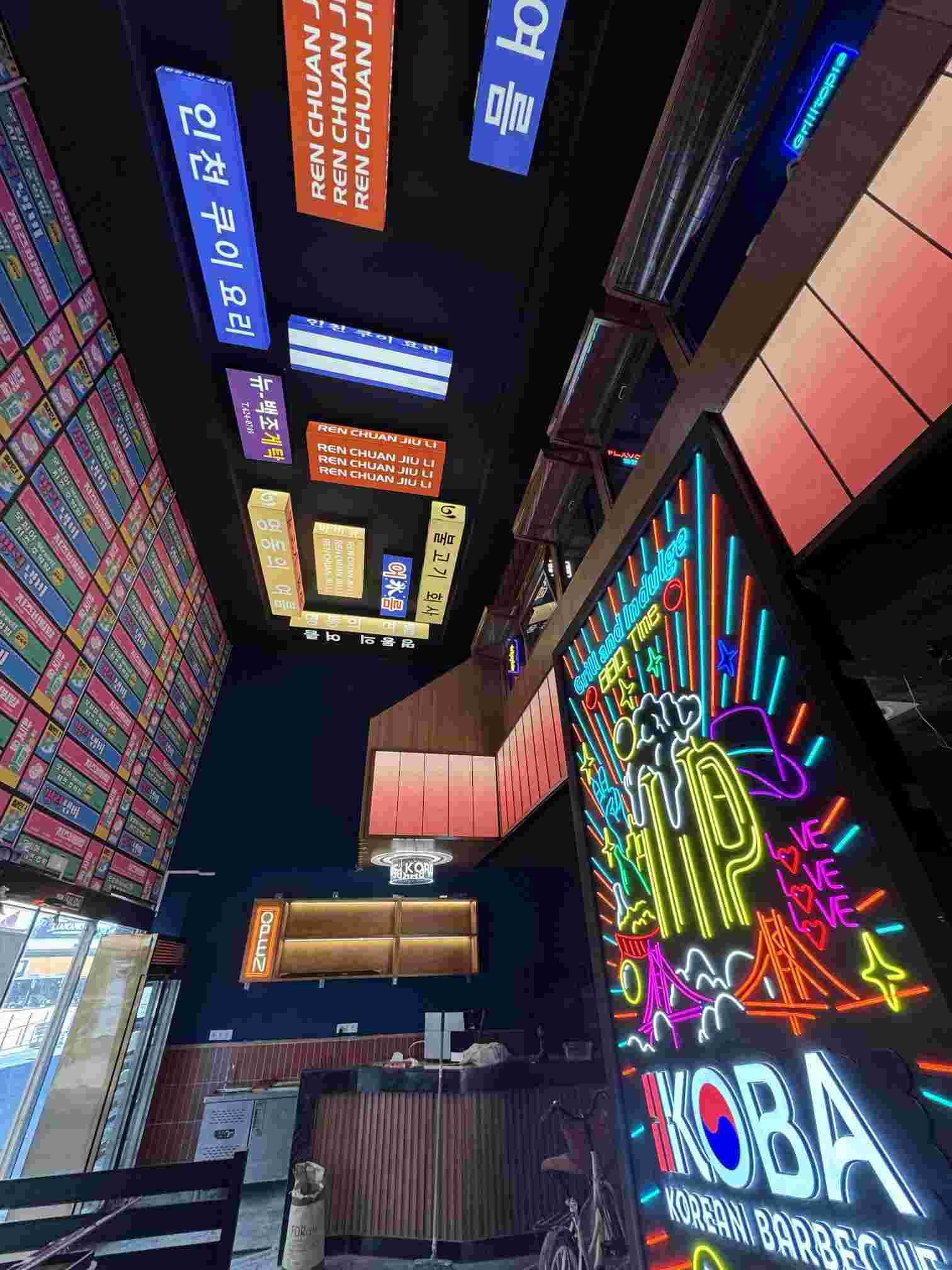 Interior de un restaurante coreano con letreros de neón y decoración colorida.