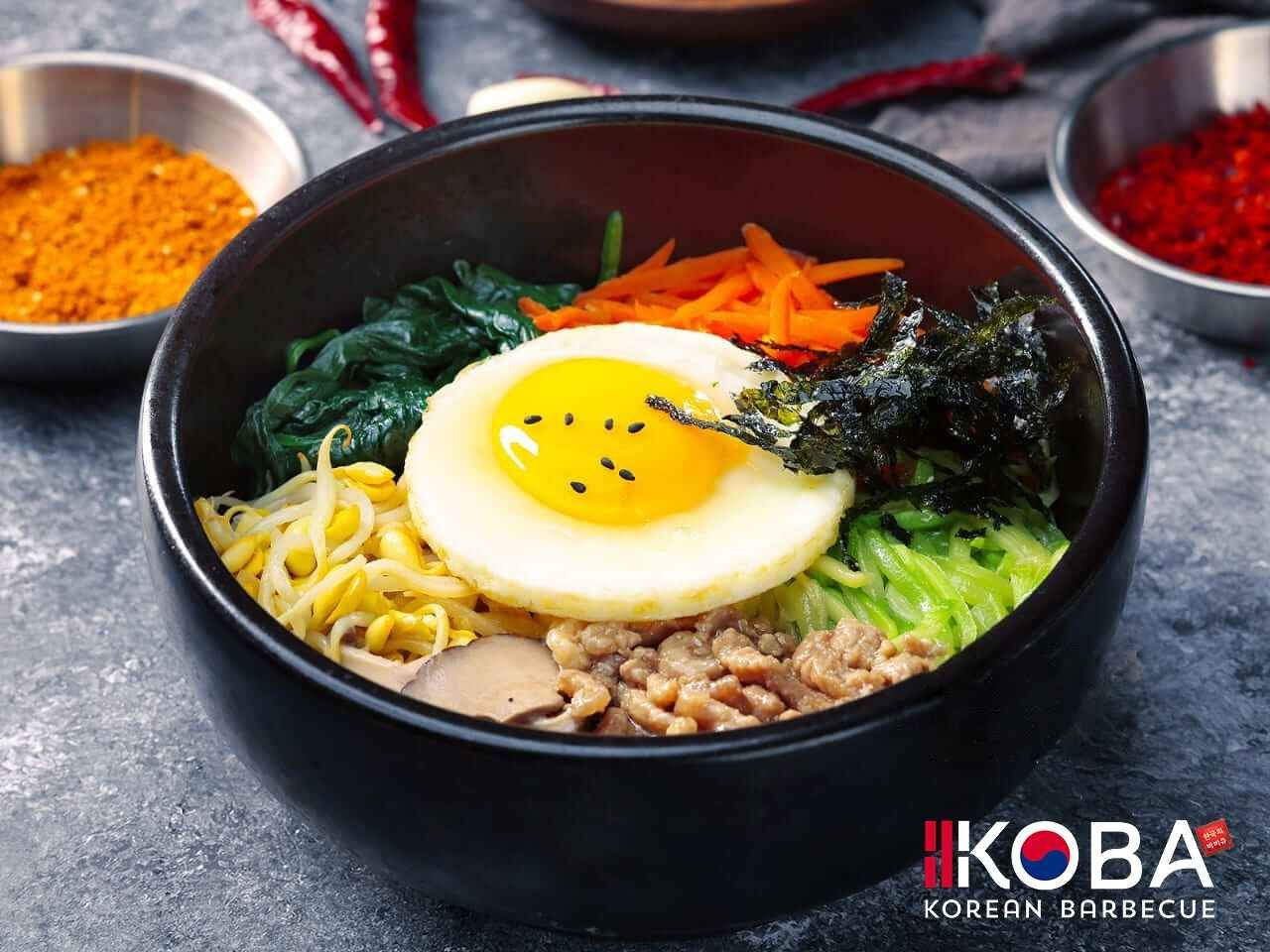 Bibimbap, tazón de arroz coreano con huevo, verduras, carne y algas en un tazón negro.