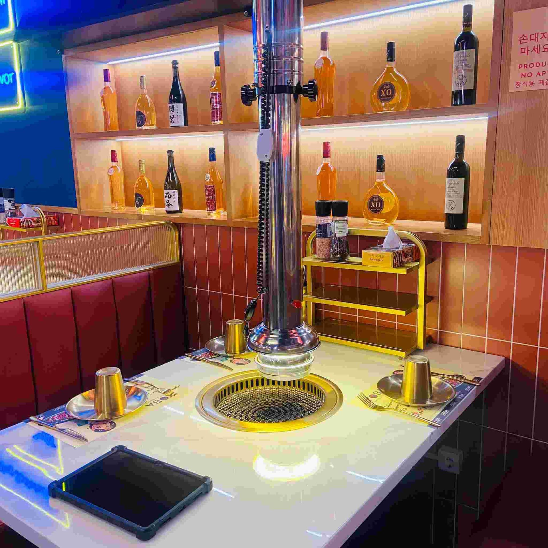 Mesa de barbacoa coreana con ventilación de acero inoxidable, botellas de alcohol y condimentos.