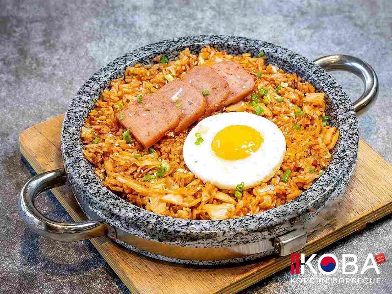 Arroz frito con kimchi, huevo frito y spam en un recipiente de piedra.