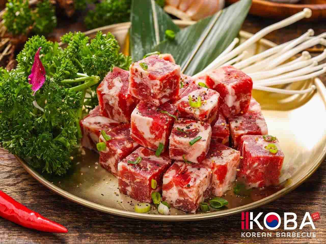 Carne de res cruda cortada en cubos, dispuesta en un plato dorado, adornada con verduras y hongos enoki.