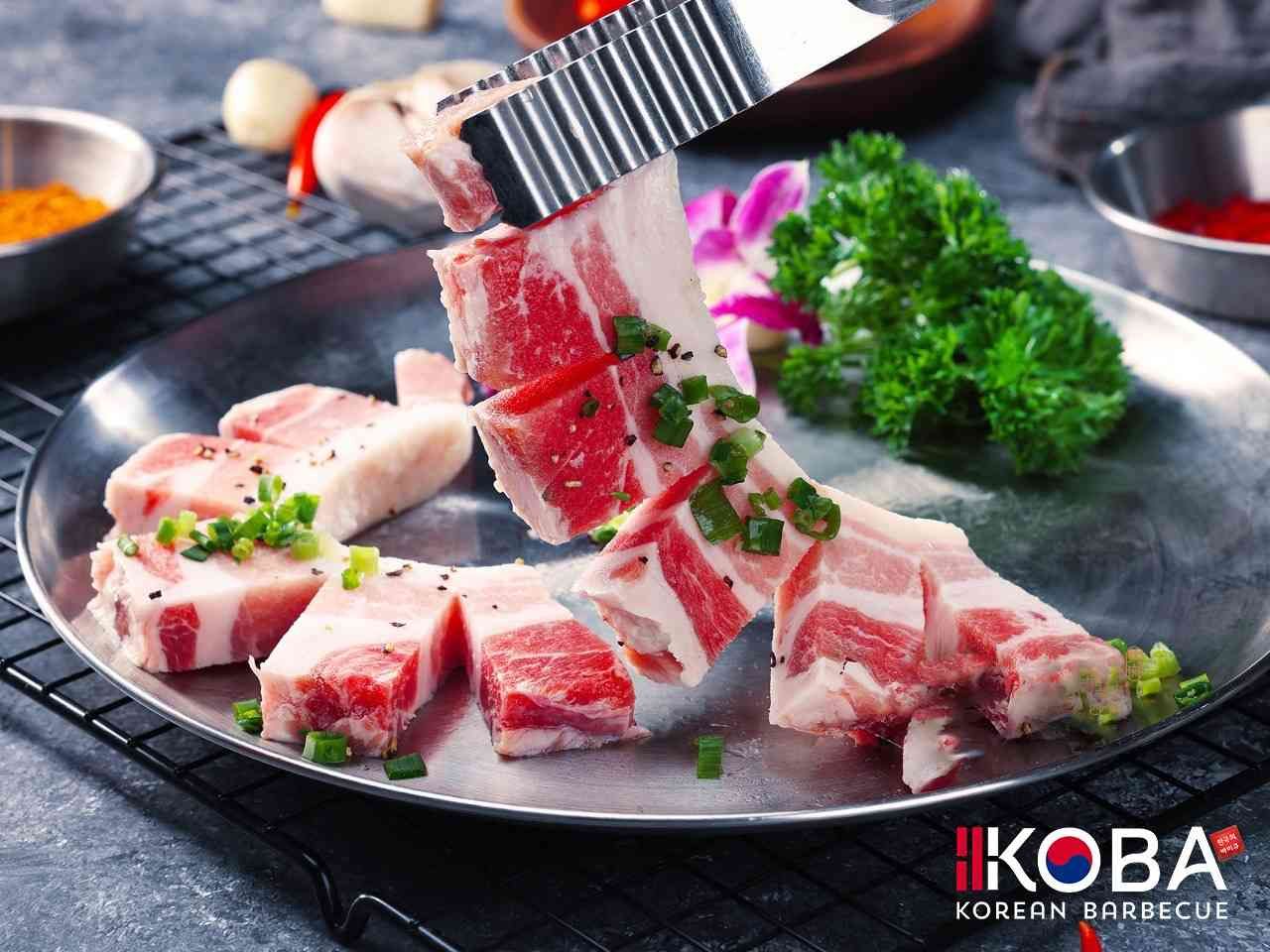 Rebanadas de panceta de cerdo cruda sobre una placa de metal, giradas con pinzas, listas para asar.