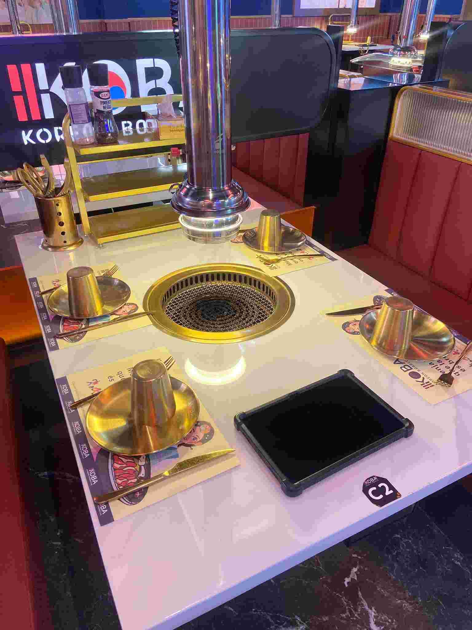 Una mesa de barbacoa coreana para cenar con parrilla, cubiertos y ventilación en un restaurante.