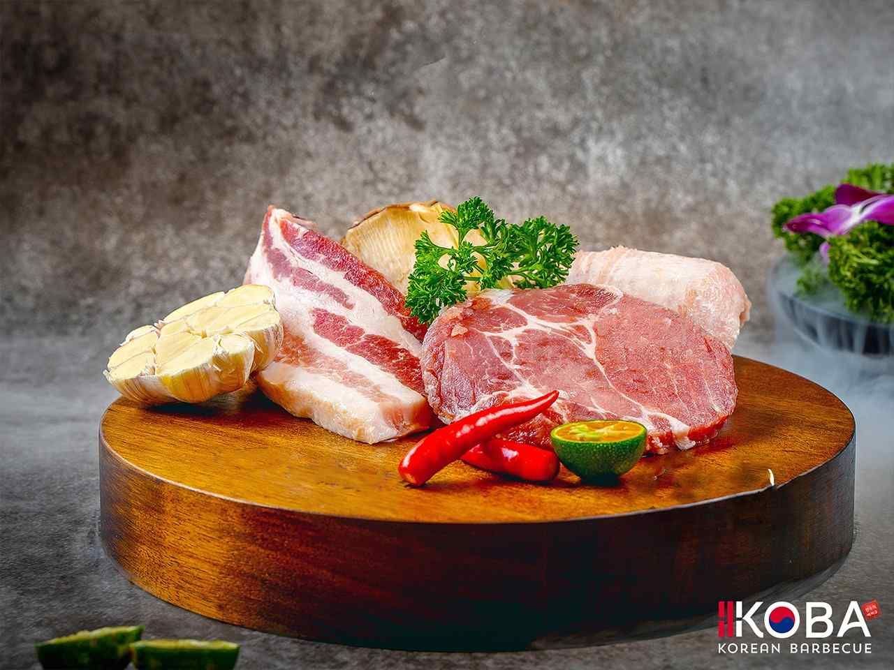 Cortes de carne sobre una tabla de madera, con ajo, chiles y hierbas. Fondo gris ahumado.