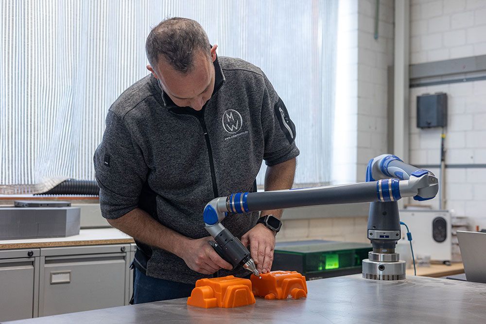 Drei orangefarbene, 3D-gedruckte Objekte befinden sich über Aluminiumformen. Die Formen weisen detaillierte Vertiefungen auf.