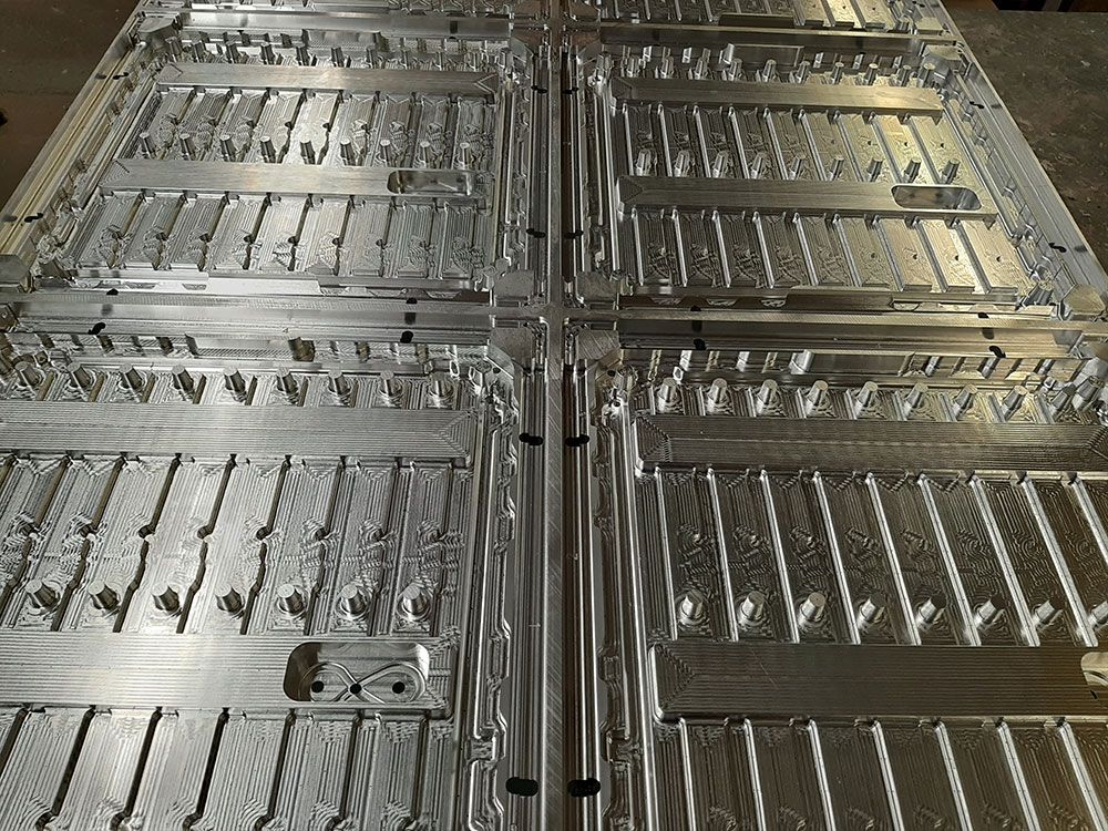 Rechteckige, silberfarbene Metallform mit asymmetrischer, stilisierter T-Form. Die Form steht auf einer Palette.