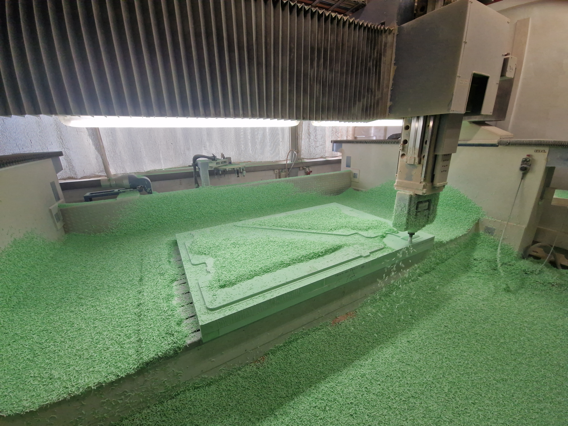 Eine CNC-Maschine schneidet eine gebogene Form aus einem grünen Schaumstoffblock; Nahaufnahme des Schneidwerkzeugs.