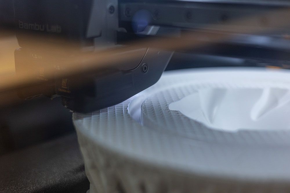 Ein 3D-Druckkopf trägt weißen Kunststoff auf ein teilweise gedrucktes weißes Objekt auf.