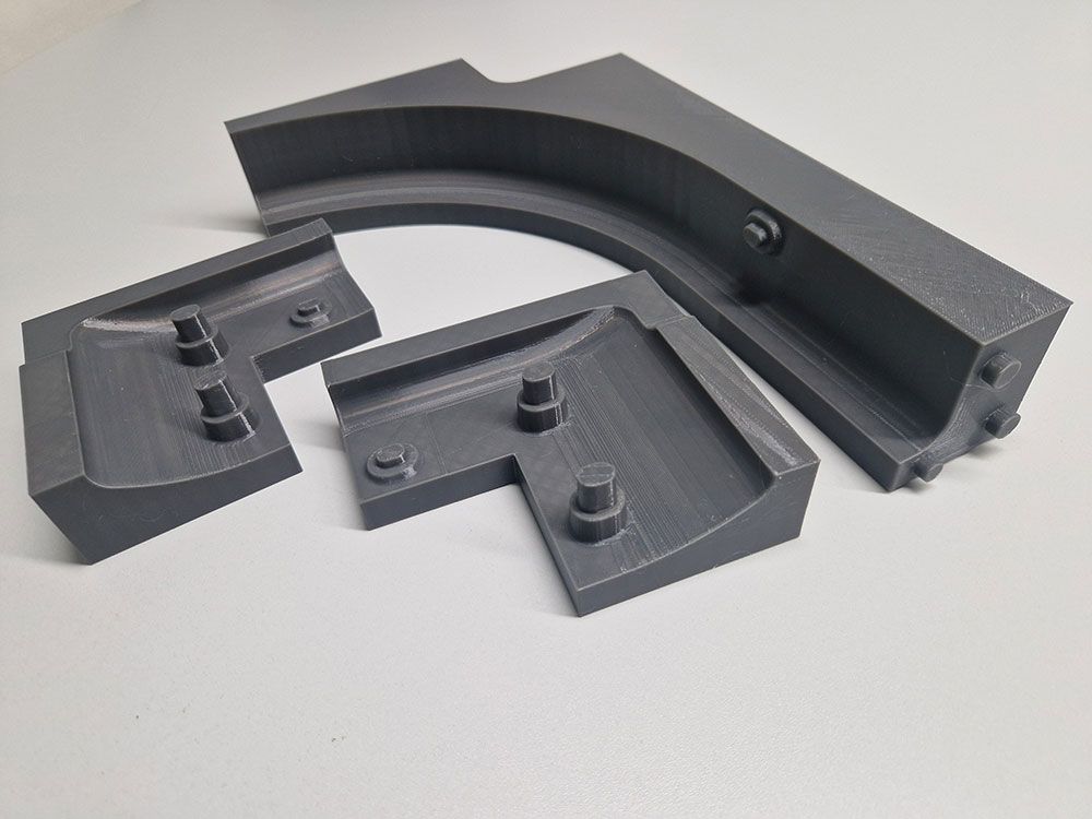 Dunkelgraue, 3D-gedruckte Box mit baumartigen Stützstrukturen an der Unterkante; auf einem weißen Schreibtisch platziert.