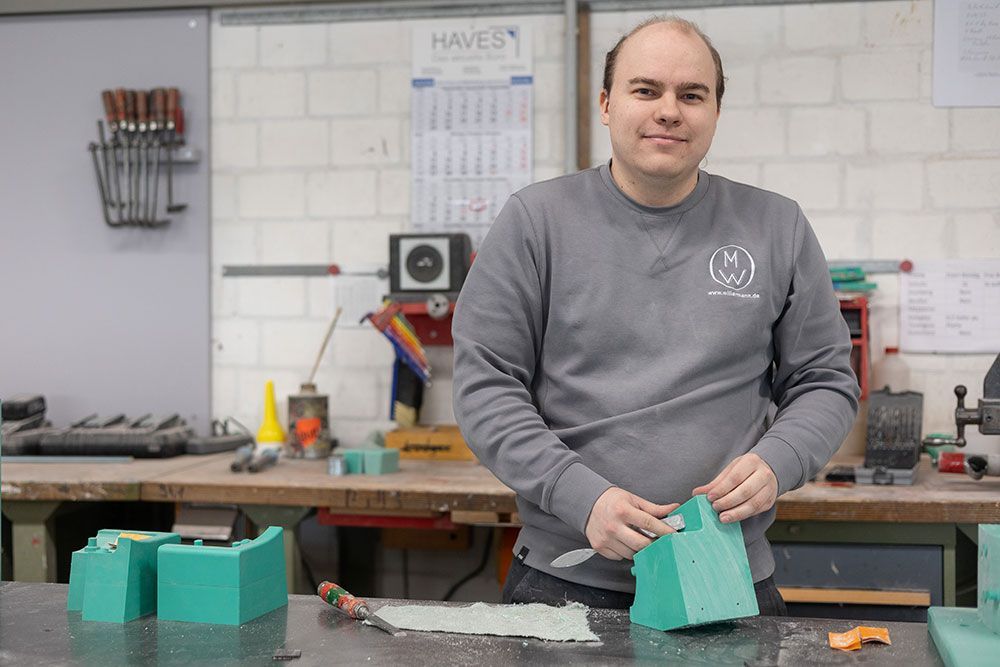 Mann in grauem Sweatshirt schnitzt grünen Schaumstoff an einer Werkbank in einer Werkstatt.