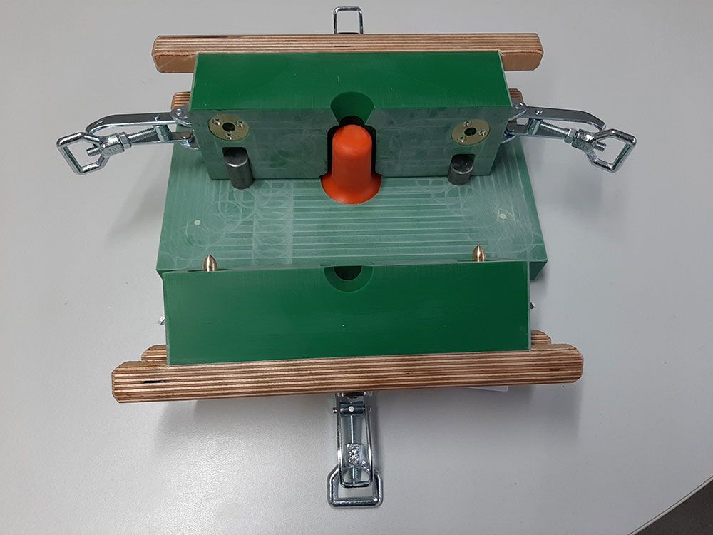 Grüne und hölzerne Formteile werden mit einem orangefarbenen Kegel zusammengeklemmt.