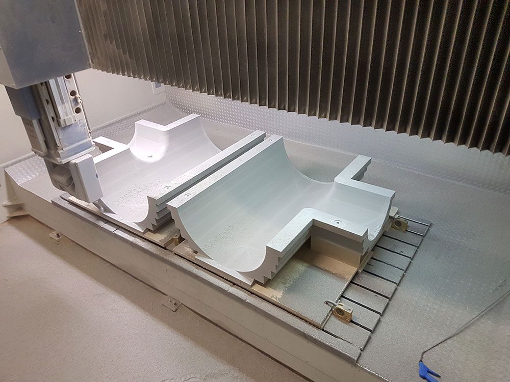 Eine CNC-Maschine schneidet zwei weiße, gebogene Industrieteile.