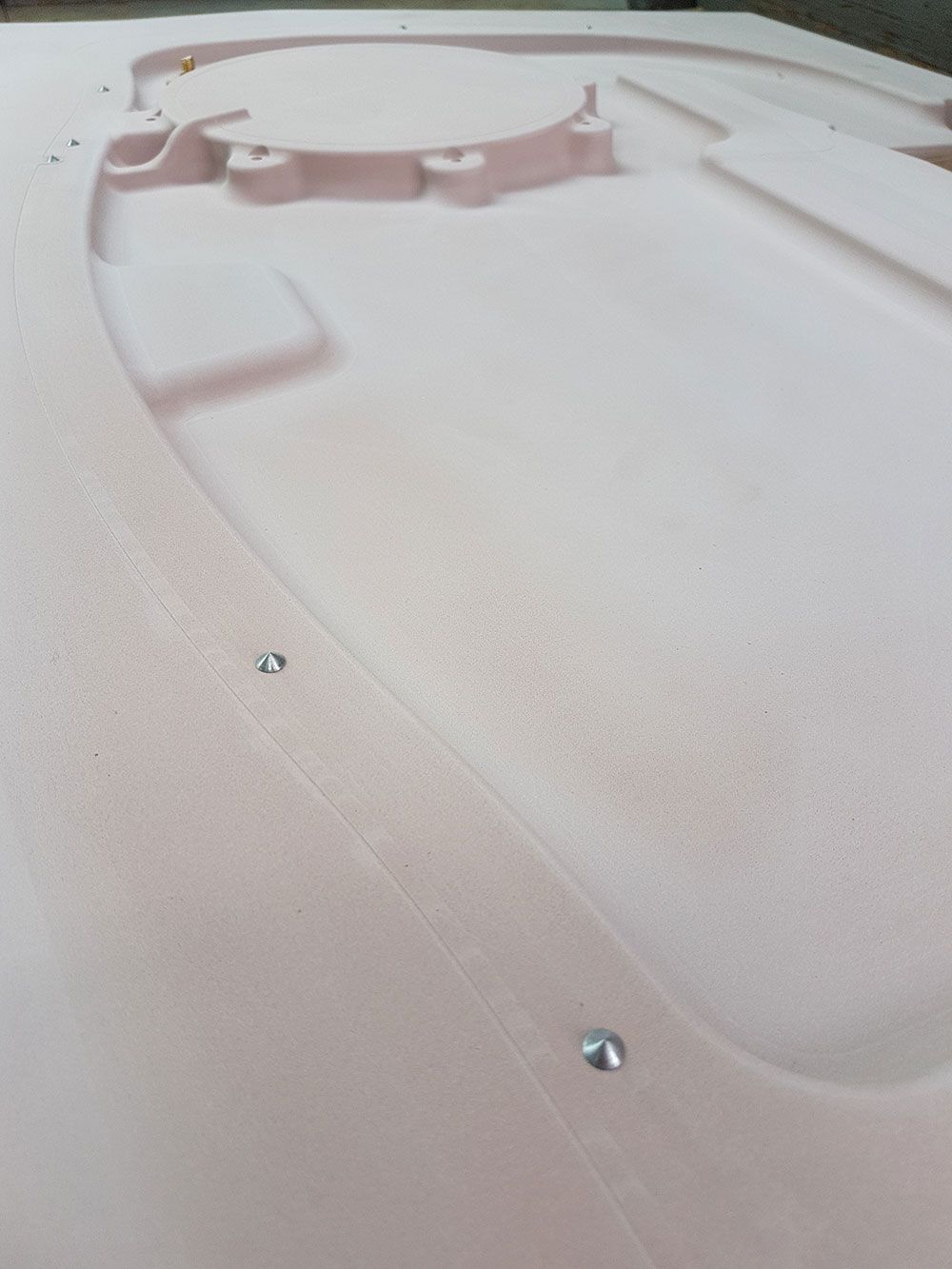 Nahaufnahme eines hellrosa, geformten Schaumstoffobjekts mit eingebetteten Metallbefestigungen und verschiedenen Details.