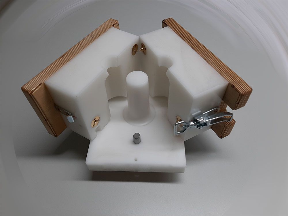 Weiße Kunststoffform mit Holzstützen, fest verschlossen, wahrscheinlich zum Gießen einer zylindrischen Form.
