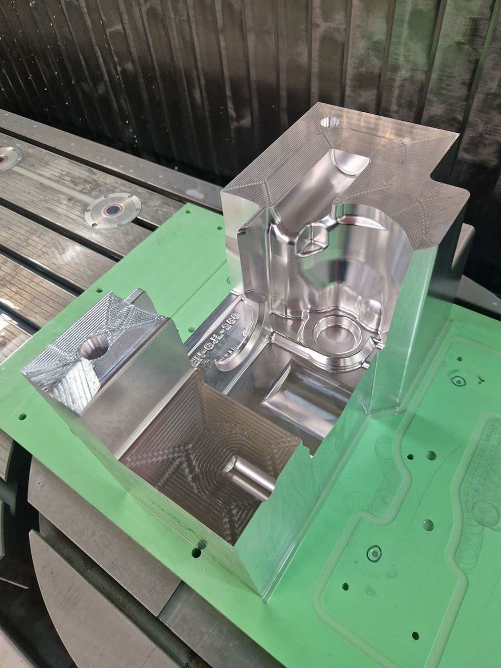 Ein bearbeitetes Aluminiumteil, das in einer CNC-Maschine auf einer grünen Spannplatte befestigt ist.