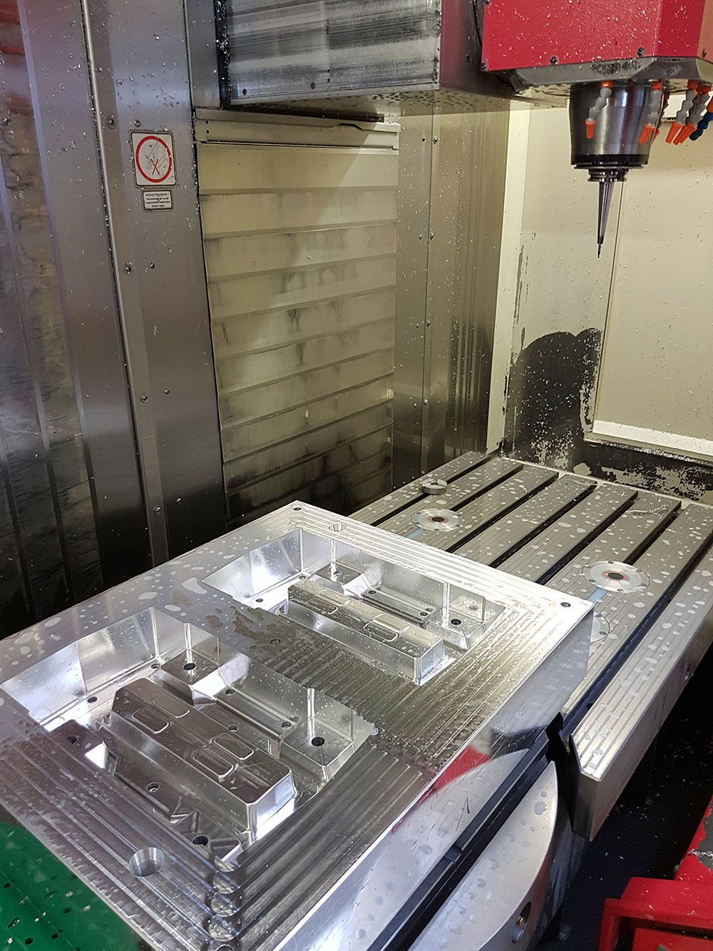 CNC-Maschine bearbeitet ein Metallteil, Wassersprühnebel vorhanden.