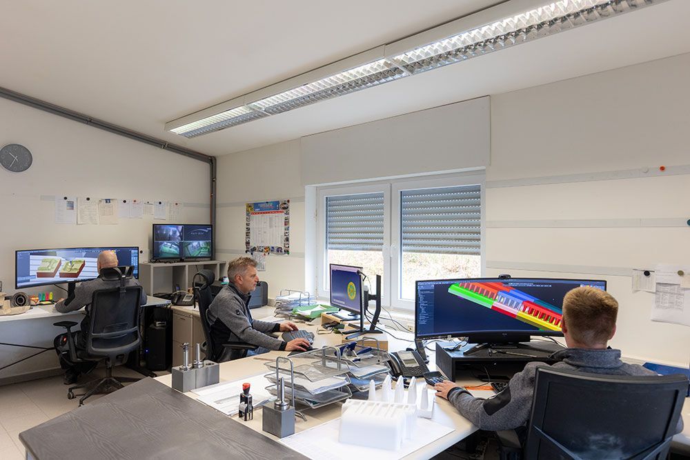 Drei Personen arbeiten in einem hellen Büro an Computern.