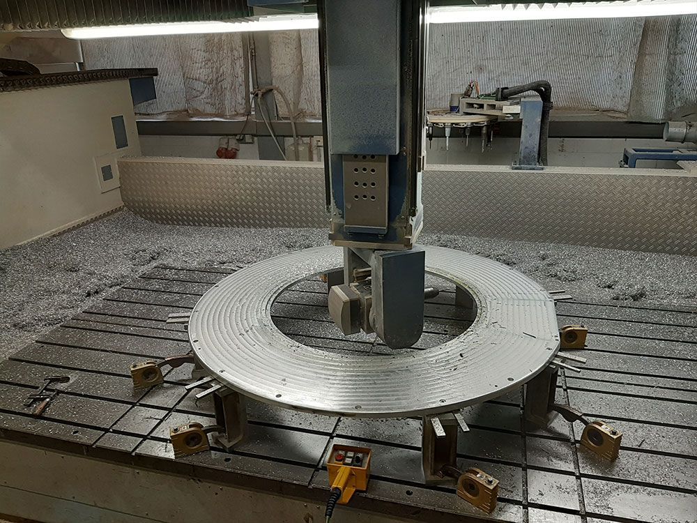 Eine CNC-Maschine schneidet ein großes, kreisförmiges Metallteil, das von Metallspänen umgeben ist.