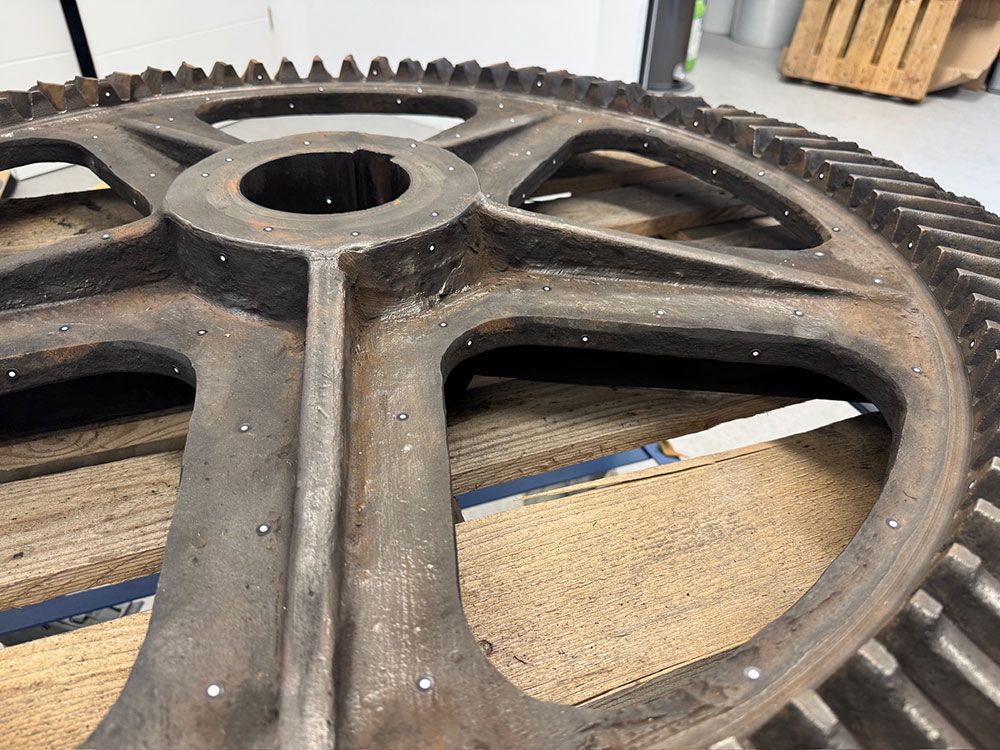 Ein Mann hält ein weißes, 3D-gedrucktes Teil in der Hand und lächelt in die Kamera. Er befindet sich in einem Büro.