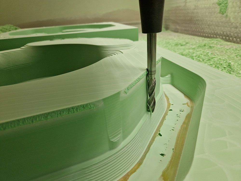 Eine CNC-Maschine schneidet eine gebogene Form aus einem grünen Schaumstoffblock; Nahaufnahme des Schneidwerkzeugs.