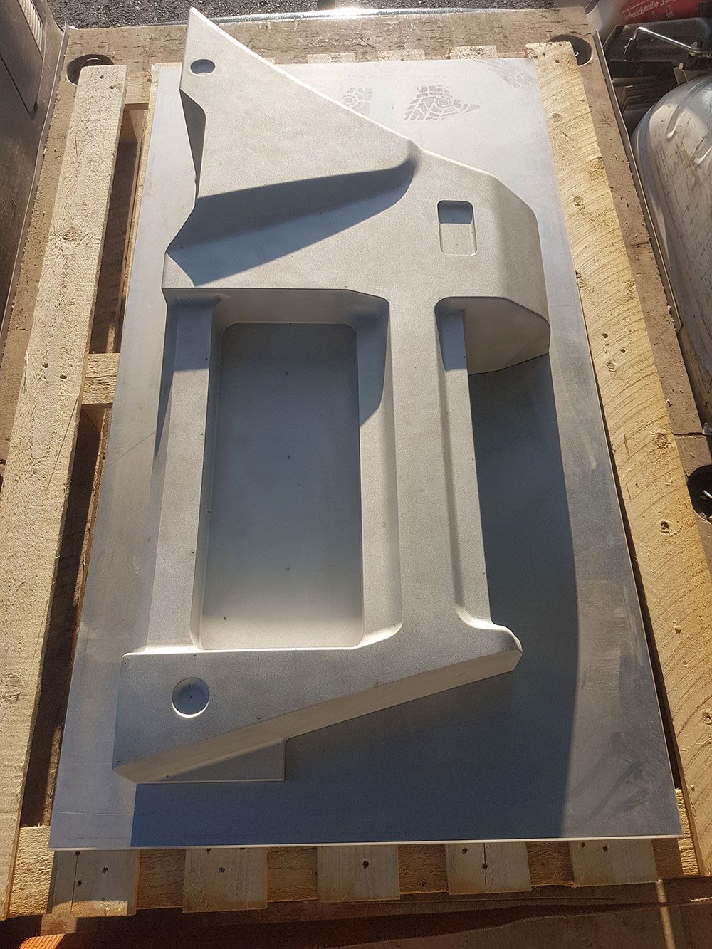 Graue Metallform auf einer Palette, geformt wie eine stilisierte Halterung, verwendet für die Fertigung.