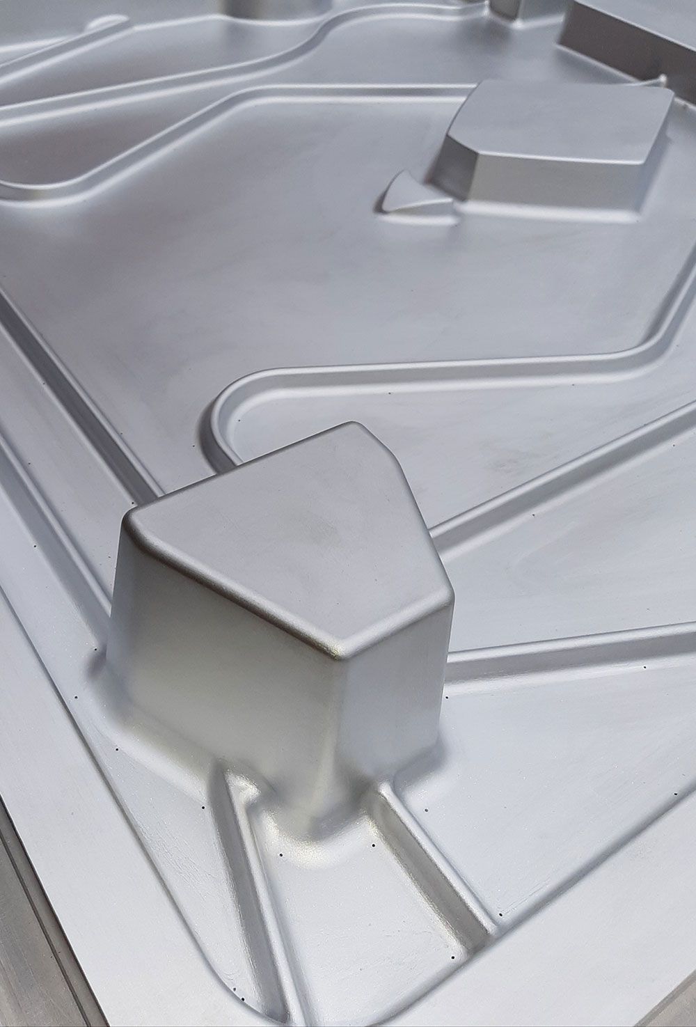 Graues Metallformteil mit geometrischen Formen und Kanälen.