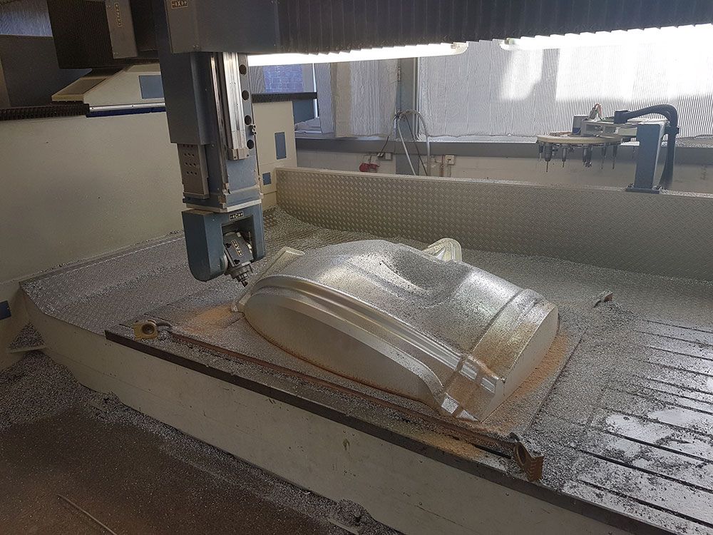 Eine CNC-Maschine fräst in einer Werkstattumgebung ein großes, helles Objekt, wahrscheinlich eine Gussform.