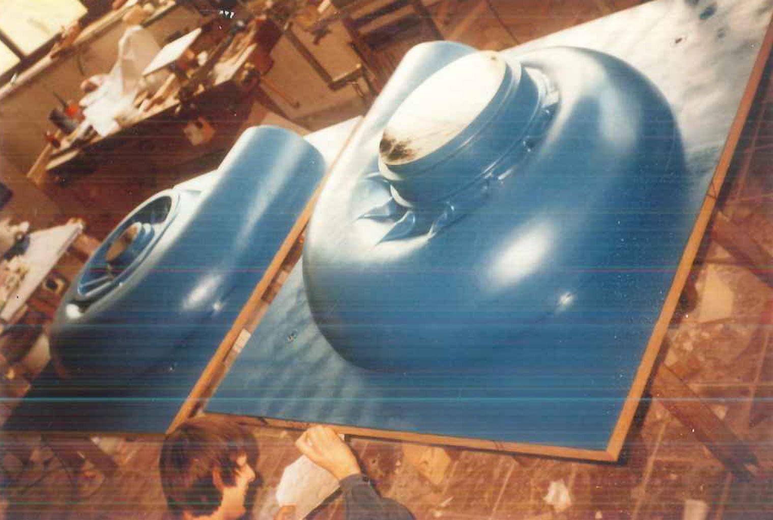 Zwei große, blaue, abgerundete Formen in Gussformen auf einer Werkbank; Person im Vordergrund.