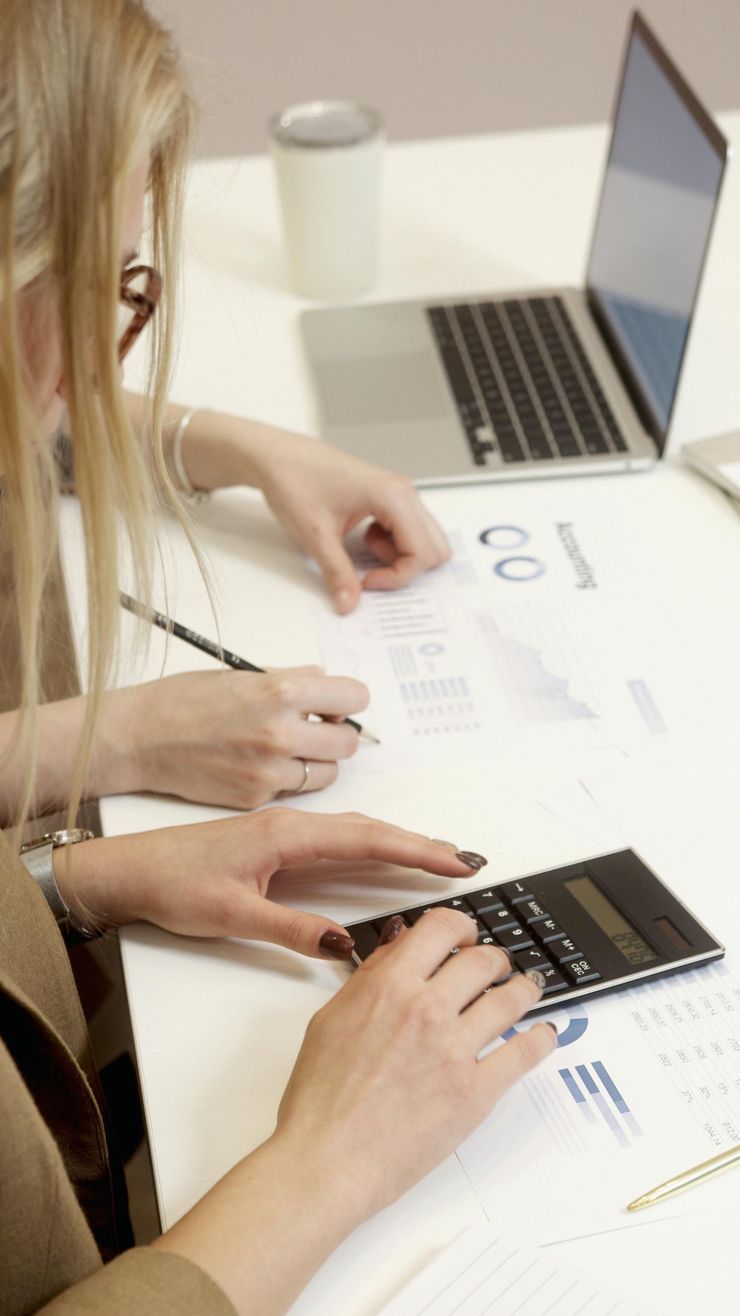 Deux personnes consultent des graphiques à un bureau, avec un ordinateur portable et une calculatrice.