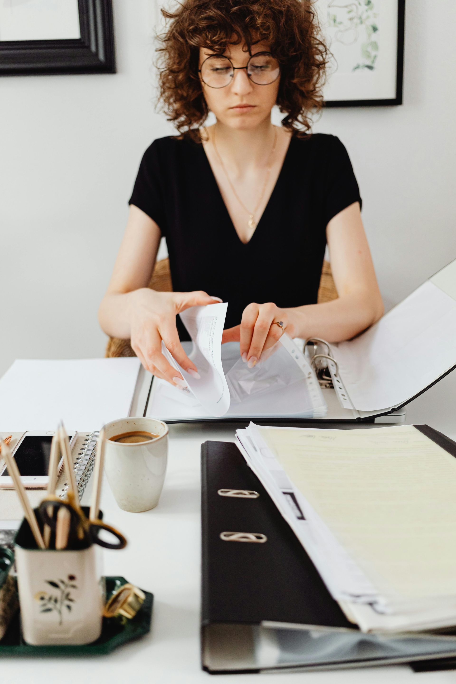 Une personne trie des papiers à un bureau, un ordinateur portable ouvert et des fournitures de bureau à disposition.
