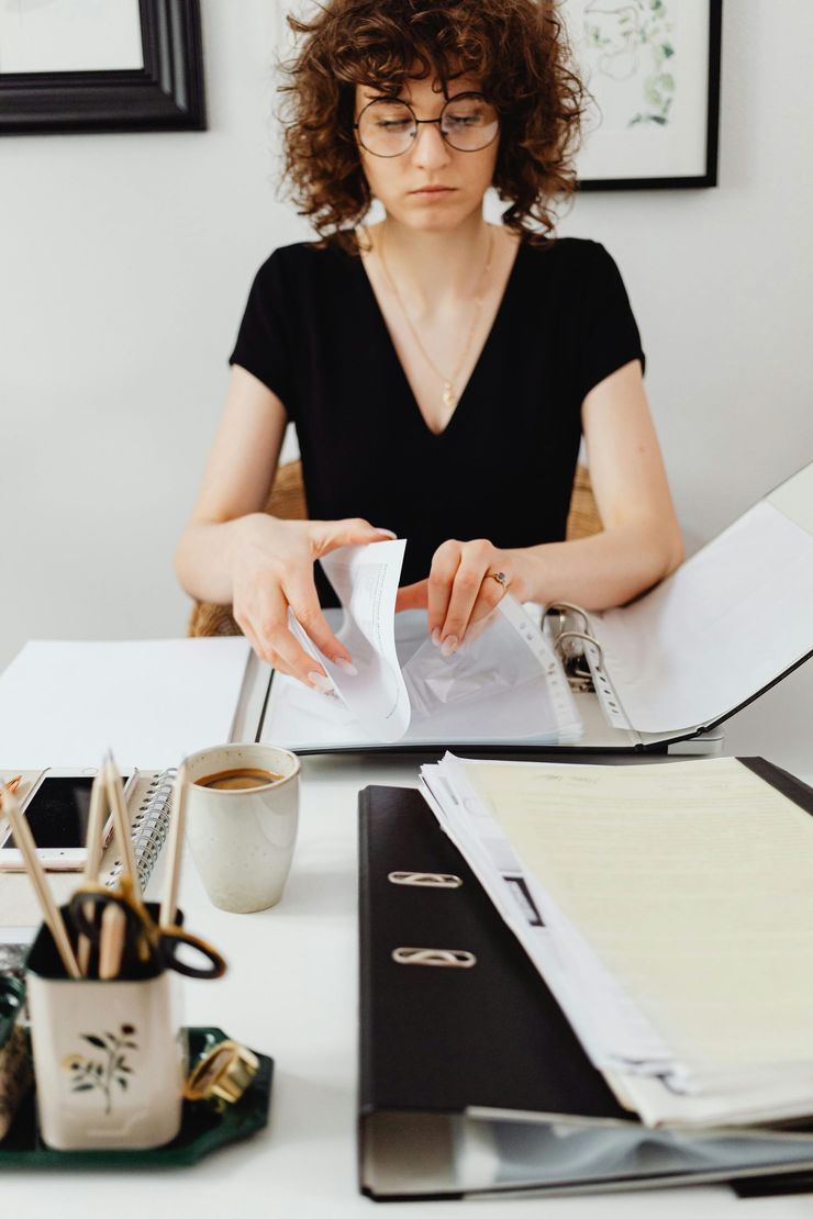 Une personne trie des papiers à un bureau, un ordinateur portable ouvert et des fournitures de bureau à disposition.