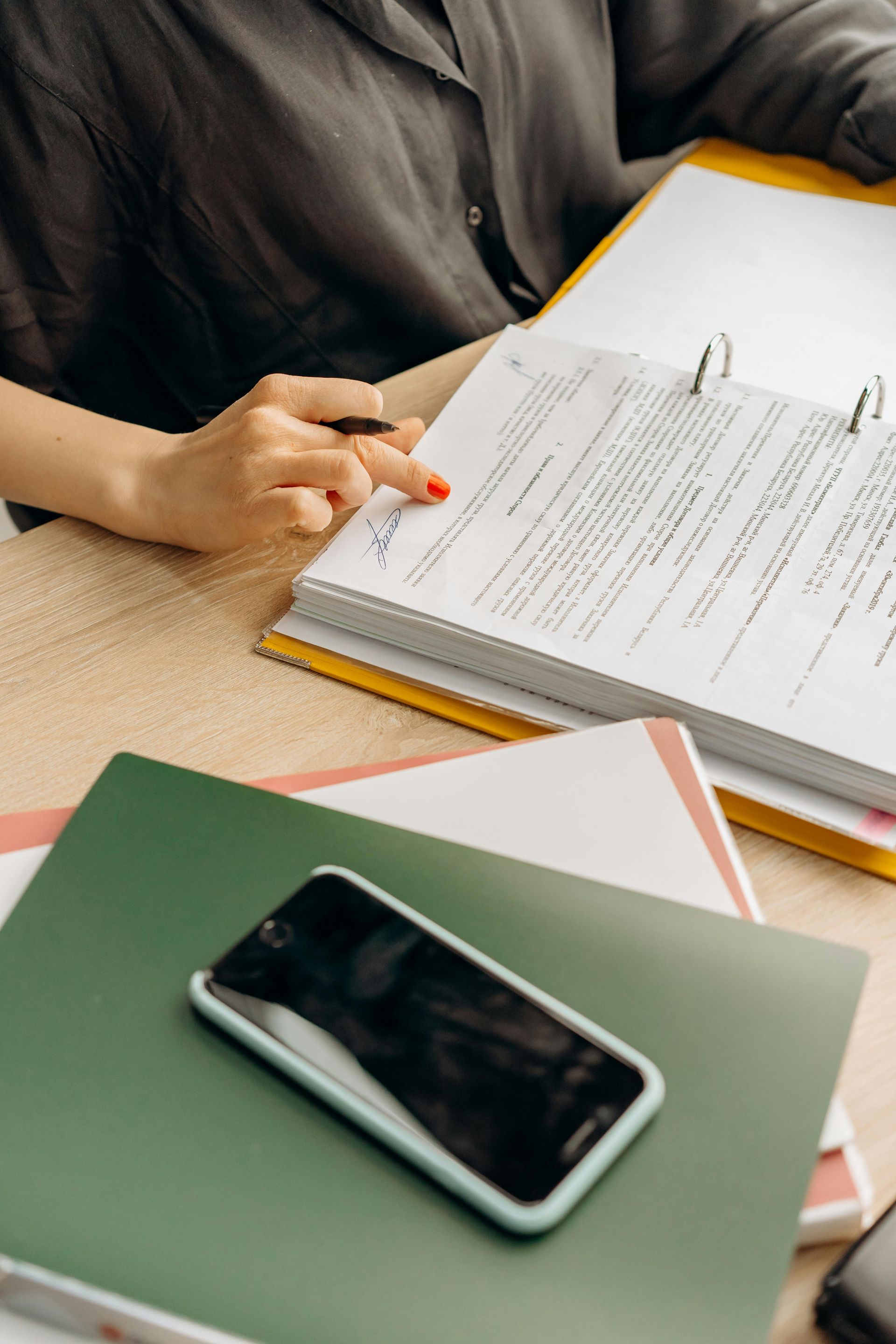 Une personne écrit sur un bloc-notes à côté d'un smartphone et d'un carnet vert posés sur une table.