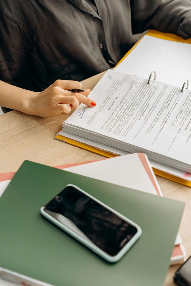 Une personne consulte des documents à son bureau, un smartphone sur un carnet vert.