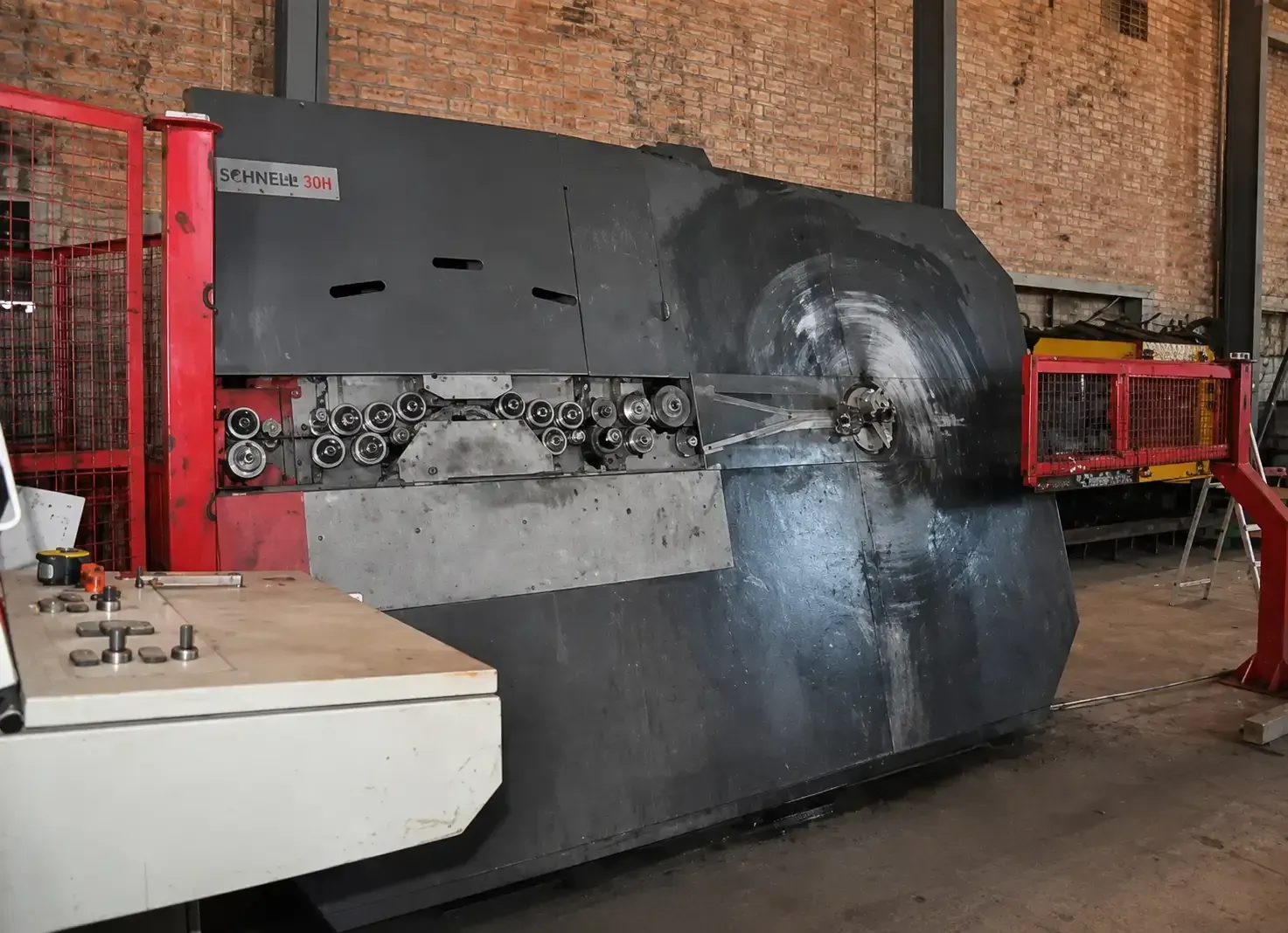 Máquina industrial con un gran tambor giratorio negro y un marco de seguridad rojo en un taller.