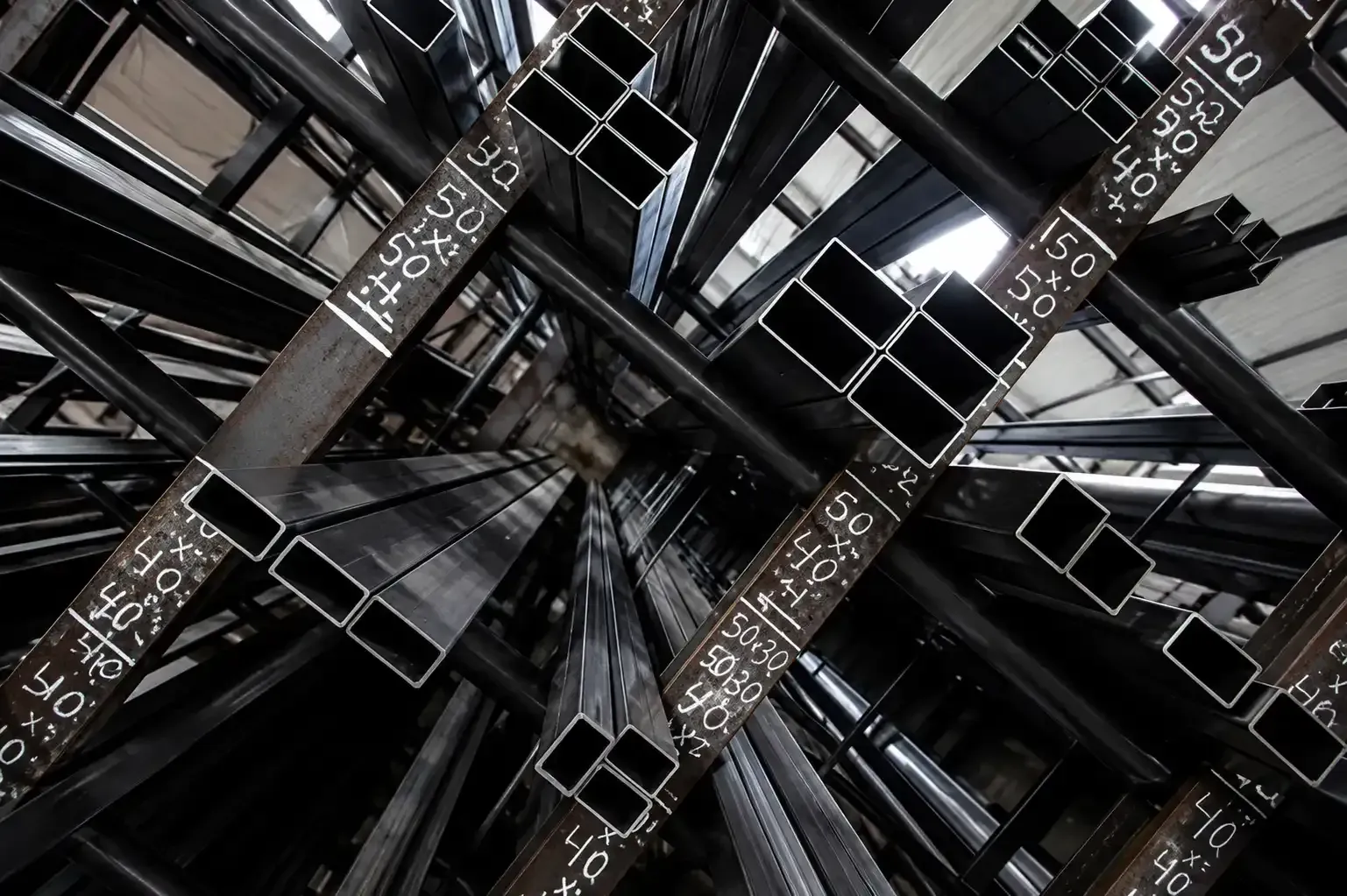 Vista abstracta de vigas de acero oscuro que se cruzan con marcas numéricas blancas en una estructura industrial.