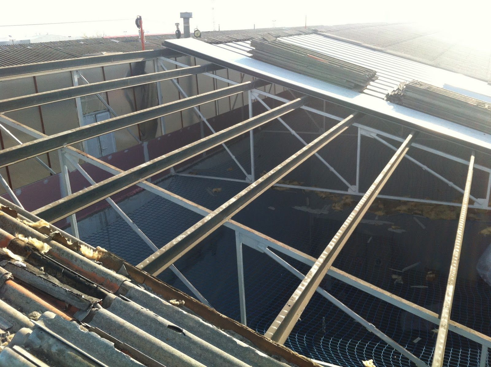 Vigas de acero de un tejado en construcción, visibles desde arriba. Luz solar.