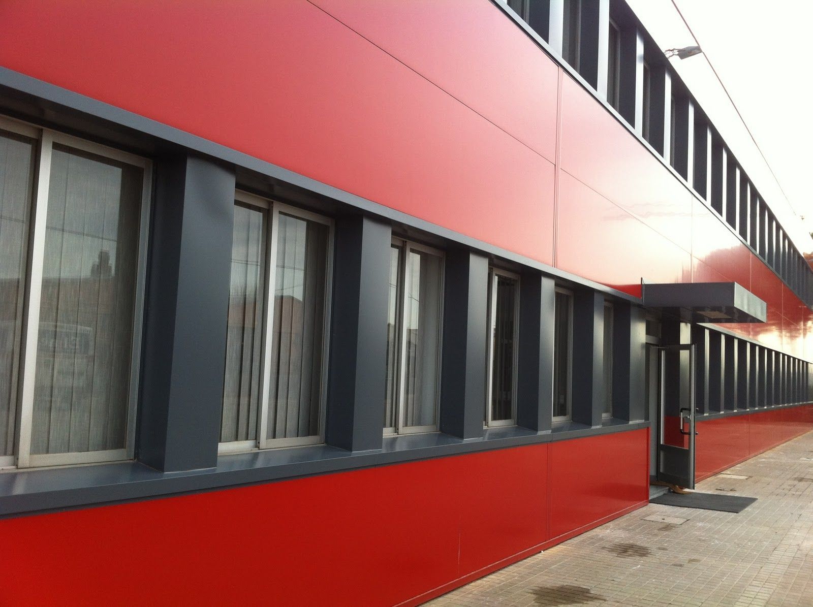 Fachada de edificio de color rojo con ventanas rectangulares enmarcadas en gris oscuro.