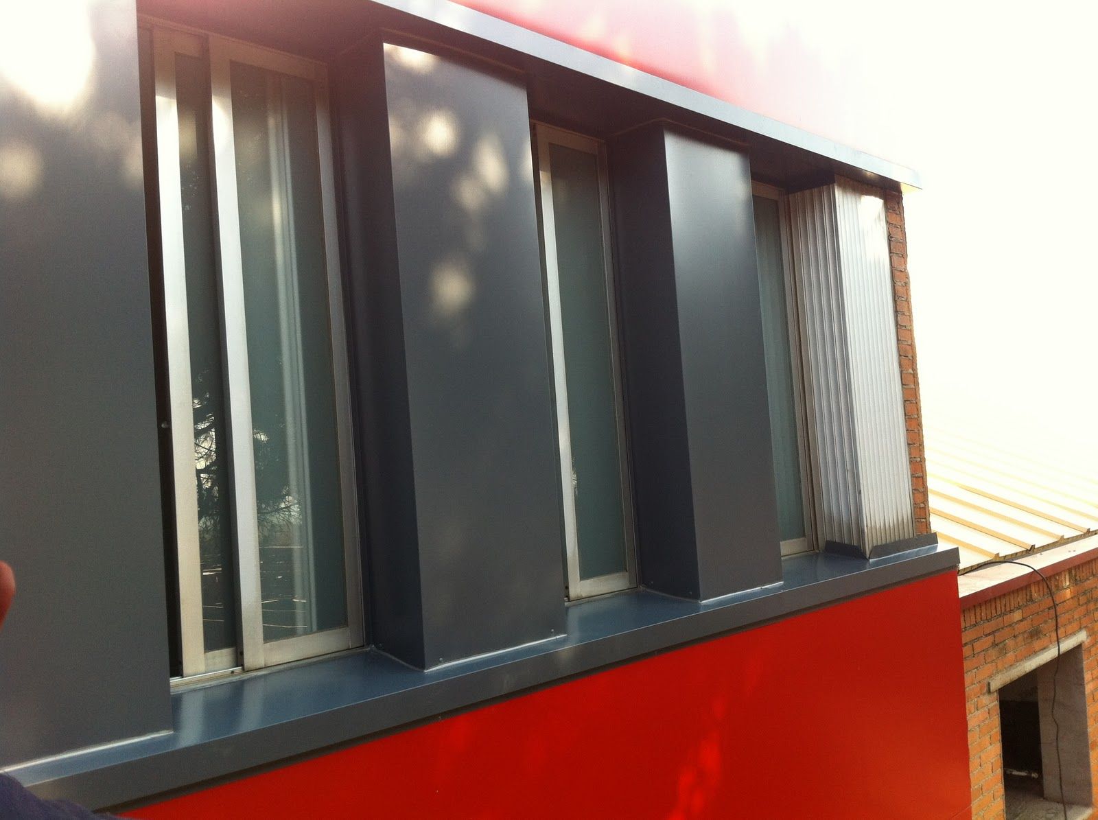 Paneles verticales de color gris oscuro junto a las ventanas de un edificio rojo y blanco.
