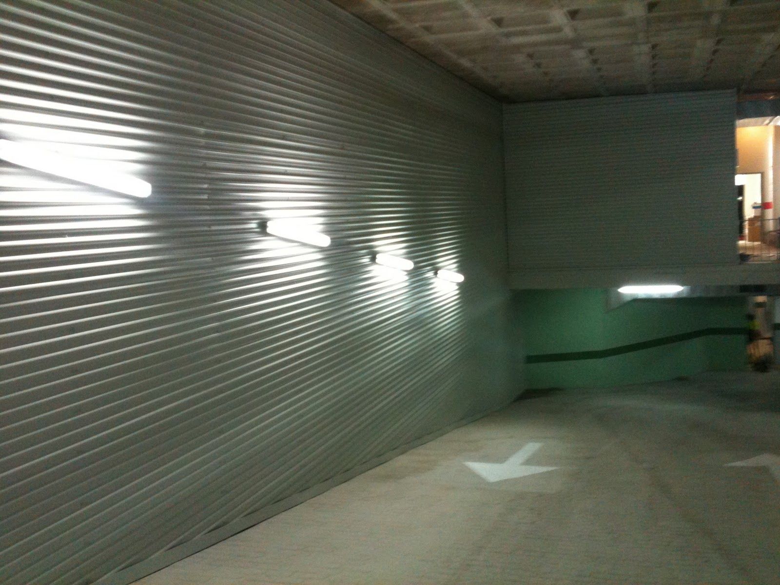 Pared de metal con luces fluorescentes en un estacionamiento; la flecha blanca indica la dirección.