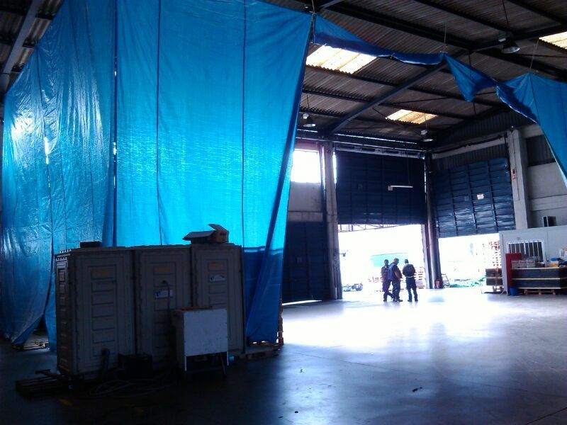 Interior de almacén con lona divisoria azul; cajas y personas visibles.