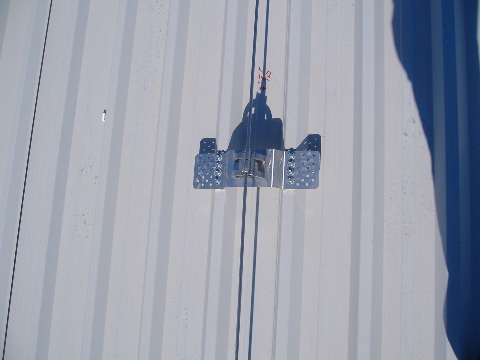 Soporte metálico fijado a una superficie corrugada de color gris claro con cables.