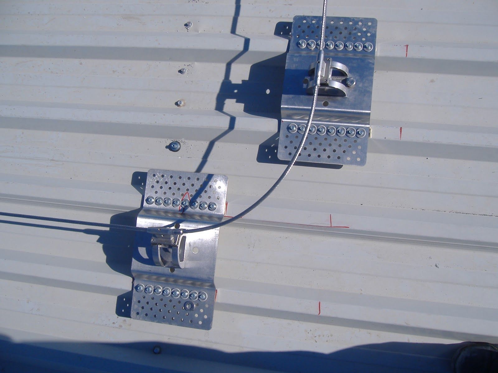 Dos anclajes de techo de metal con un cable unido a ellos, colocados sobre un techo de metal corrugado.