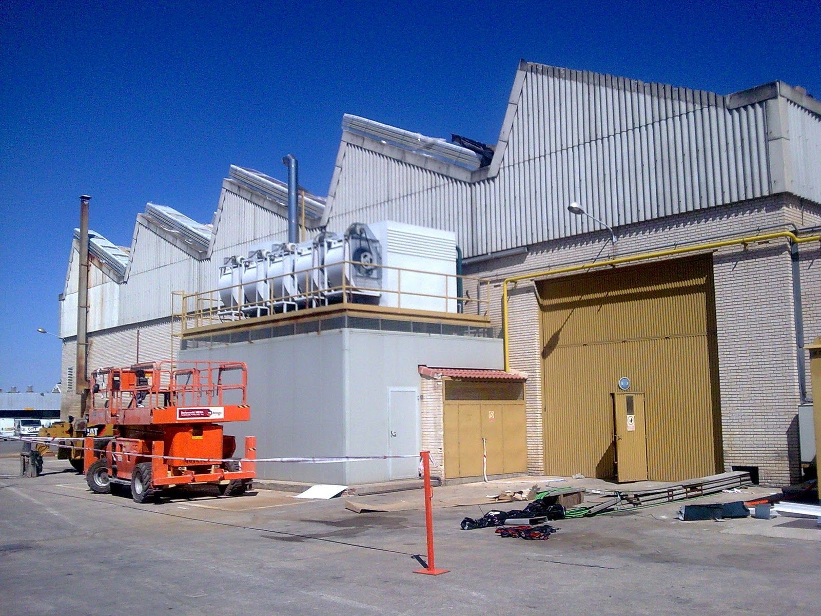 Exterior de edificio industrial con techo inclinado, puerta grande y ascensor naranja.