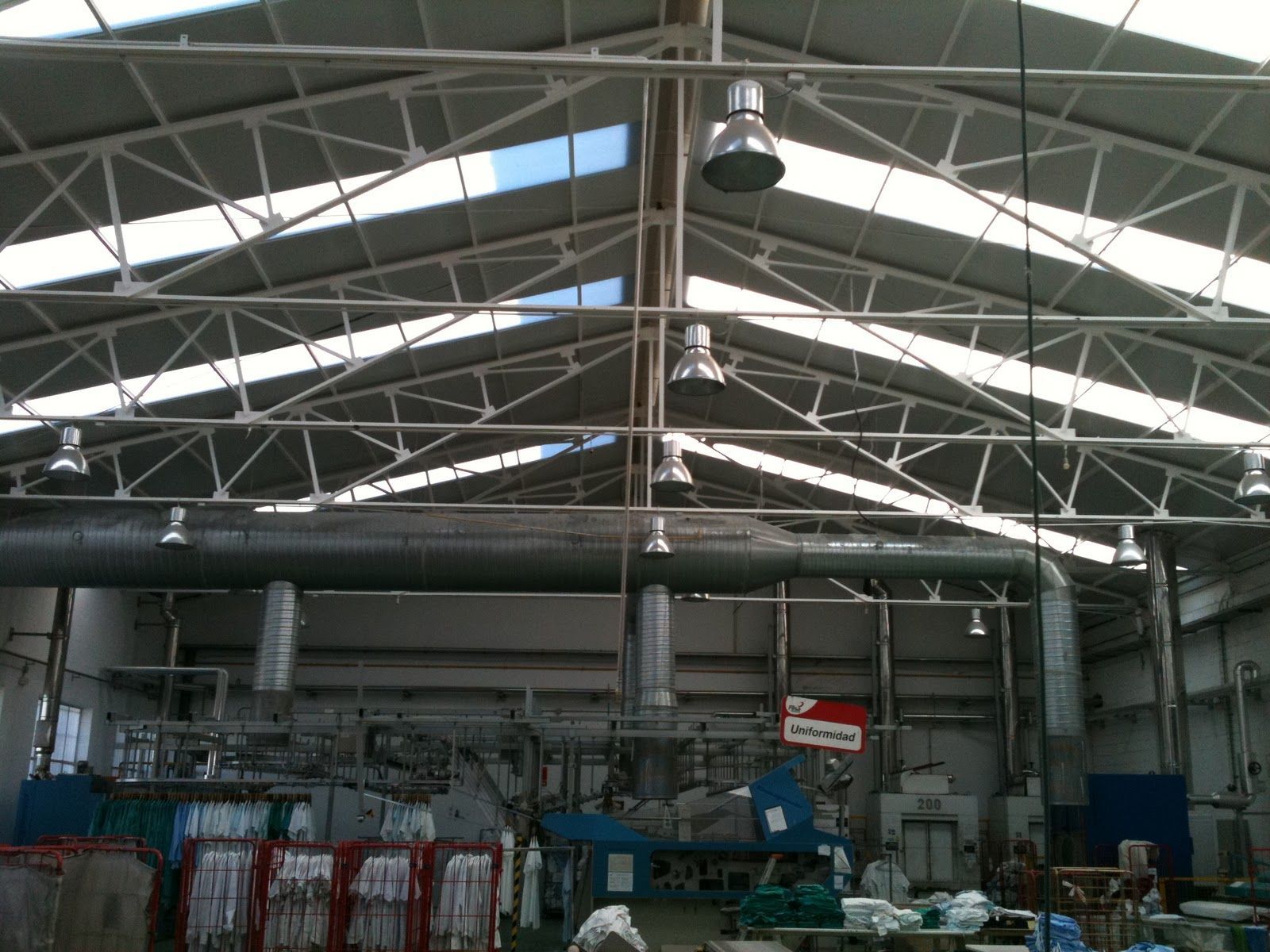 Interior de almacén con techo de armadura de acero, tragaluces, luces colgantes y maquinaria.