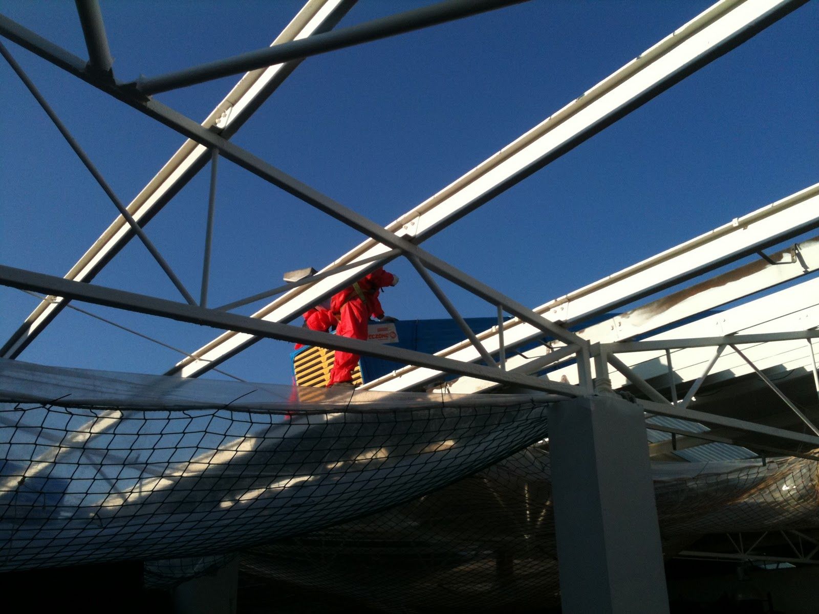 Persona con chaqueta roja trabajando en la estructura del techo bajo un cielo azul.