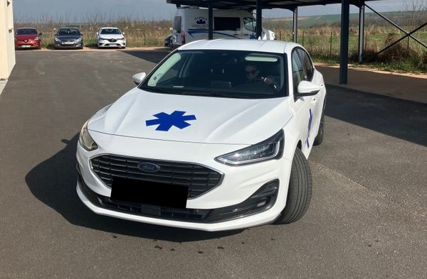 Voiture blanche avec étoile bleue, stationnée à l'extérieur.
