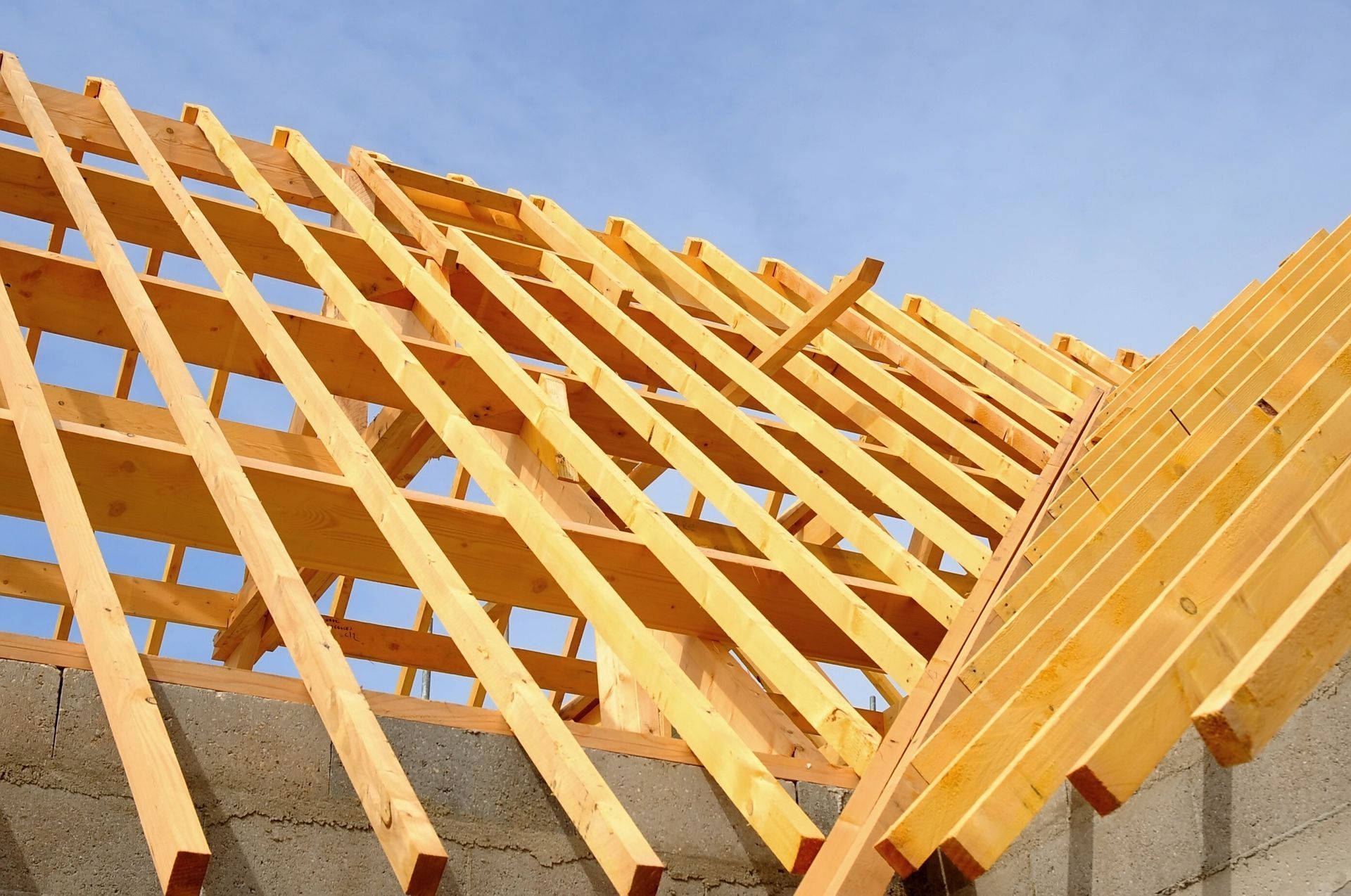 Charpente de toit en bois en construction, se détachant sur un ciel bleu au-dessus de murs en béton.
