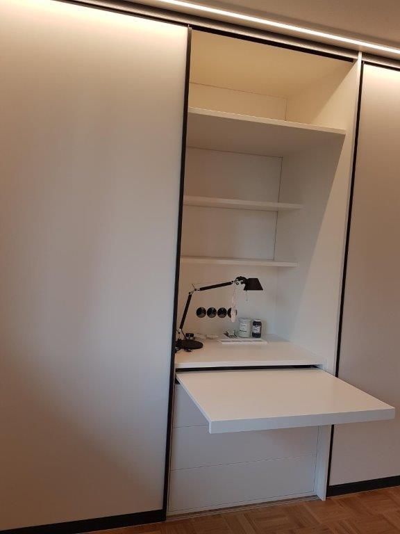 Ein Zimmer mit einem Schreibtisch und Regalen darin