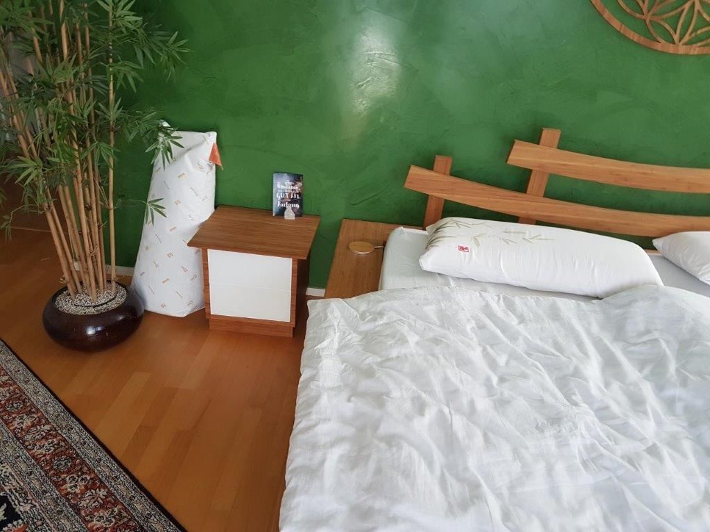 Ein Schlafzimmer mit Bett, Nachttisch und Pflanze.